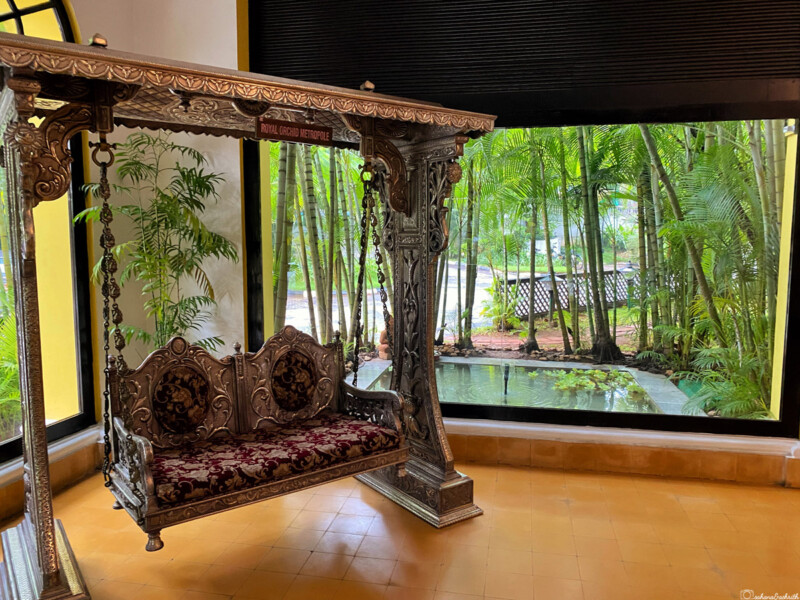 Ornate silver swing with intricate carvings placed near a large window overlooking a garden