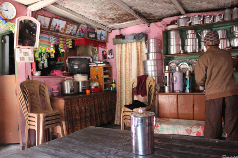 The interior of a cosy home run cafe, rustic shop with shelves of utensils, a man standing near the counter, and various items on display