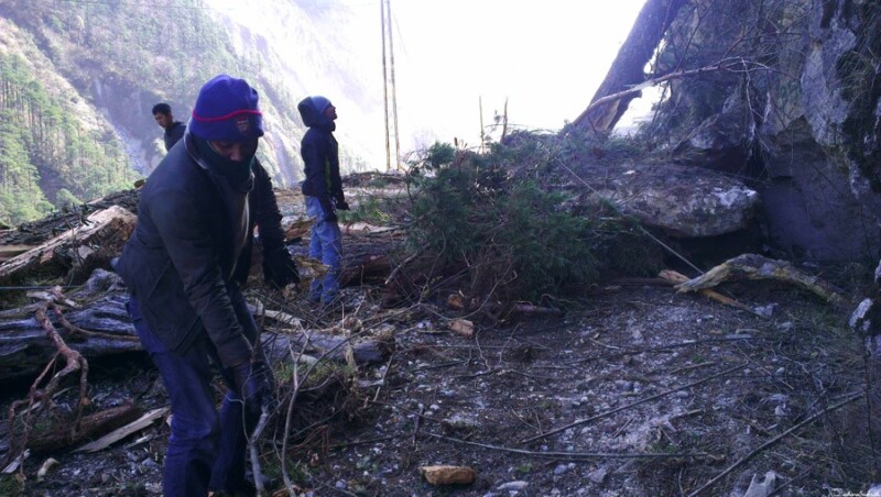 Several people work together to clear fallen trees and debris on a mountain road to North Sikkim