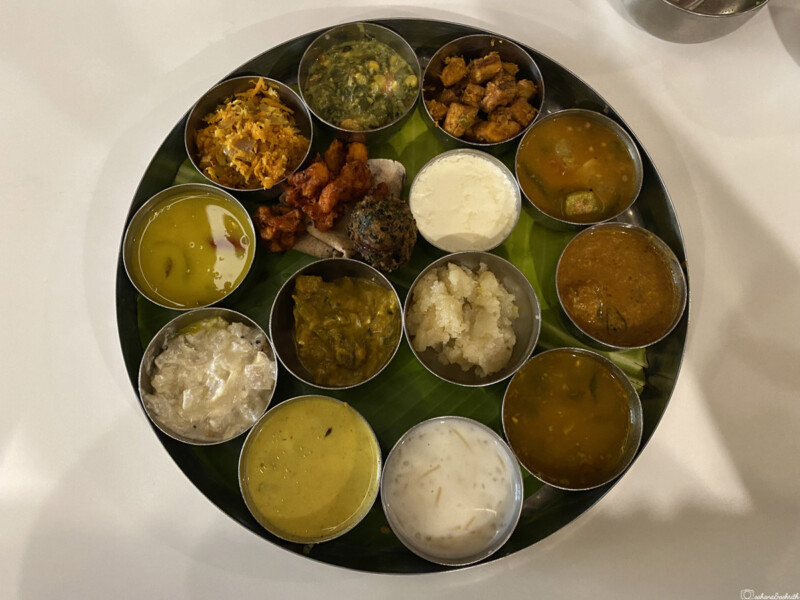 A traditional South Indian thali with various dishes in small bowls arranged on a large round tray