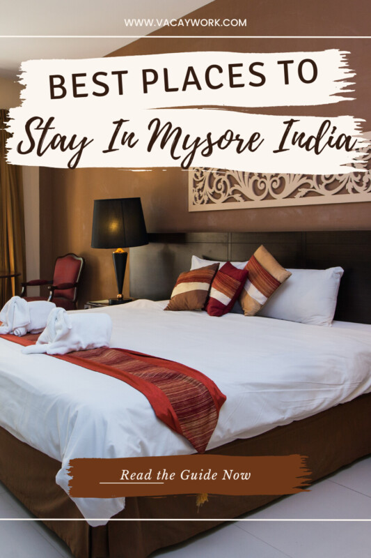 A double bed in a hotel room with pillows and towels, and ornate decor on the wall with text on it that says Best Places to Stay in Mysore India