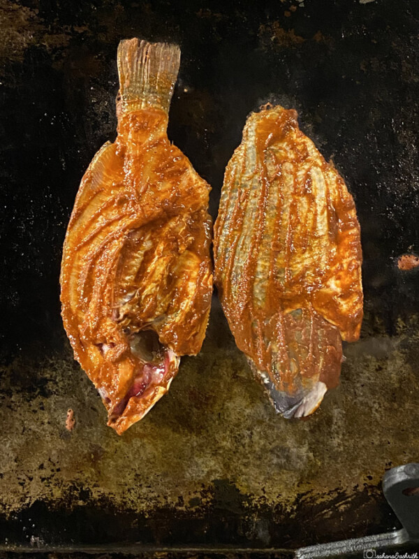 Two grilled fish on a black iron tawa
