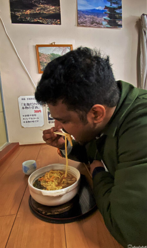 A man eating noodles with chopsticks at a small restaurant in Japan