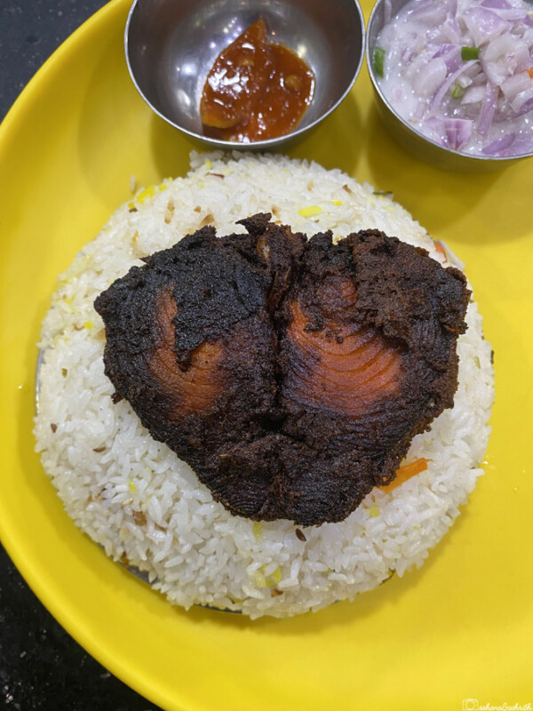 Yellow plate with rice topped with fried fish, chutney, and onions