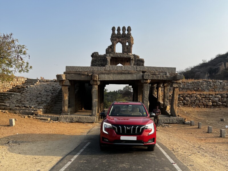 A red SUV parked in front of an ancient stone structure in Hampi, India.