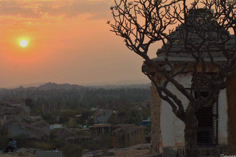 A beautiful sunset view over the landscape of Hampi with an ancient structure and tree in the foreground.