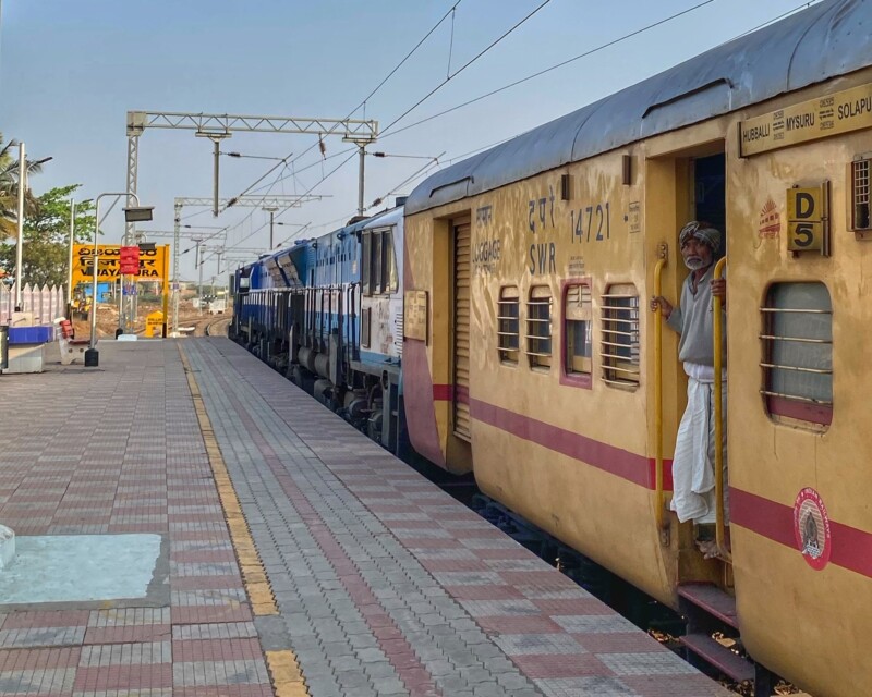 A yellow passenger train arriving at a station platform, with a man standing by the door.