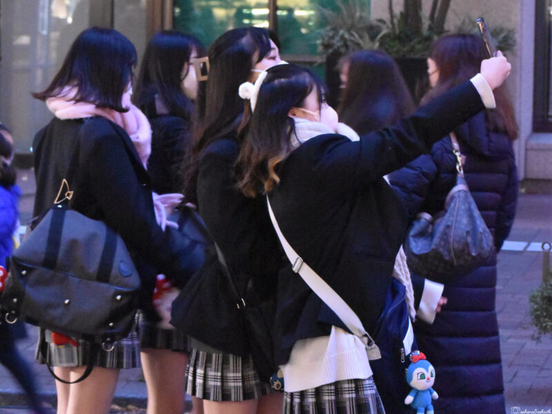 A group of schoolgirls in uniforms taking a selfie in a Japanese street, capturing a moment of friendship and fun.
