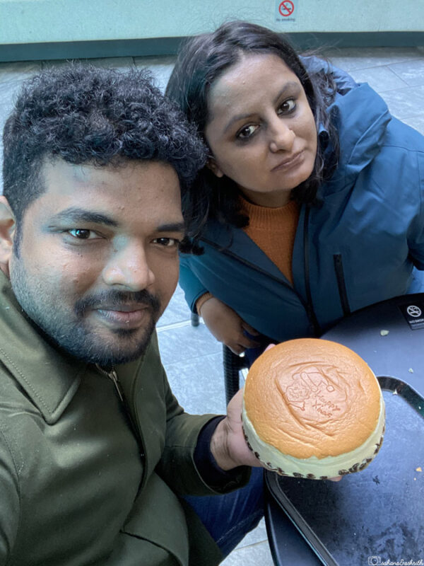 Two travellers taking a selfie with a fluffy cheesecake at a café in Japan, enjoying a popular local dessert.