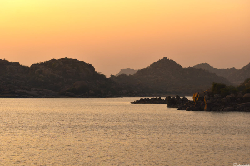 A serene river with rocky hills in the background during sunset.