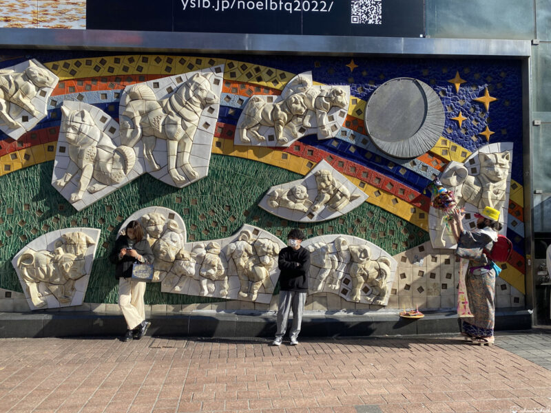 People standing in front of a colourful mosaic wall in Japan, enjoying the public art and local atmosphere.