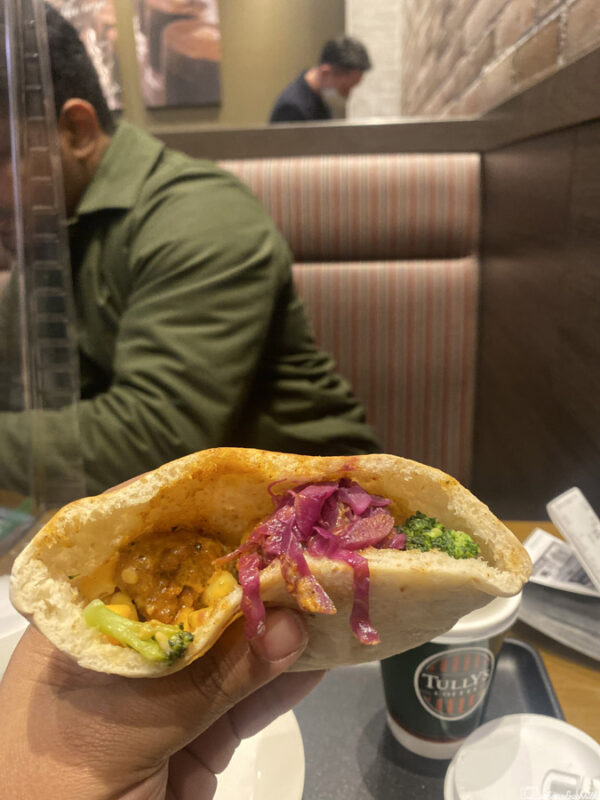 Pita bread stuffed with vegetables and pickled onions, held by a person in a café.