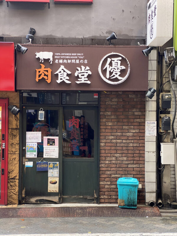 Front of a Japanese restaurant with a sign advertising 100% Japanese beef, a blue bin outside
