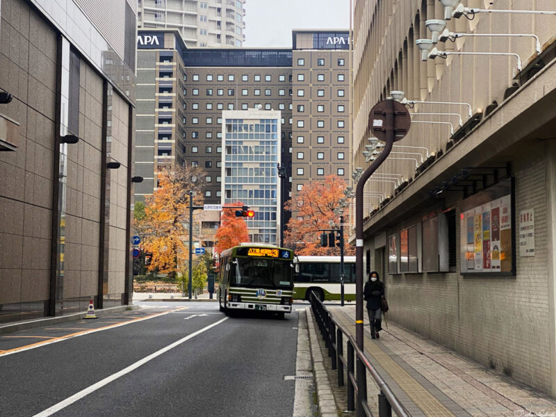 A public bus in an urban area with tall buildings and a street light.