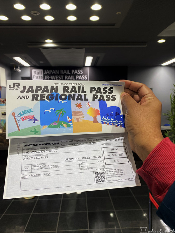 A Japan Rail Pass being held up in front of a JR ticket counter.