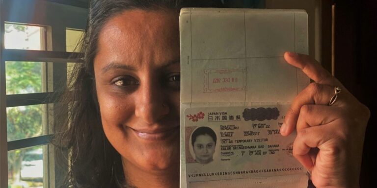 A woman smiling while holding her passport, showing a Japan tourist visa page, with natural light filtering through a window in the background.