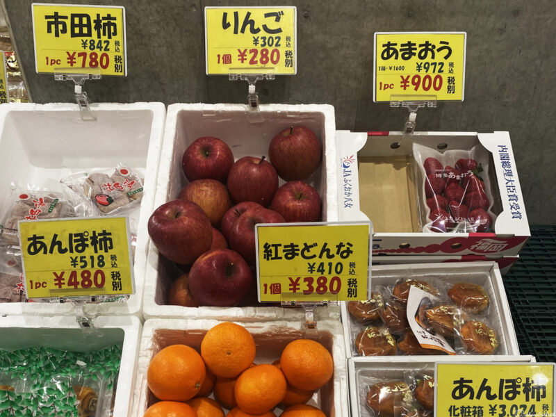 Japanese market display with various fruits, including apples, strawberries, and oranges, with prices marked in yen.