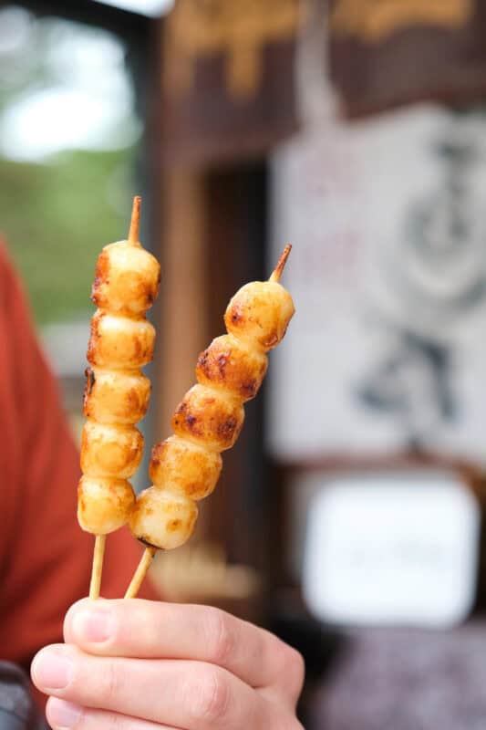 a hand holding 2 skewer sticks of mitashi dango rice balls soaked with soy sauce
