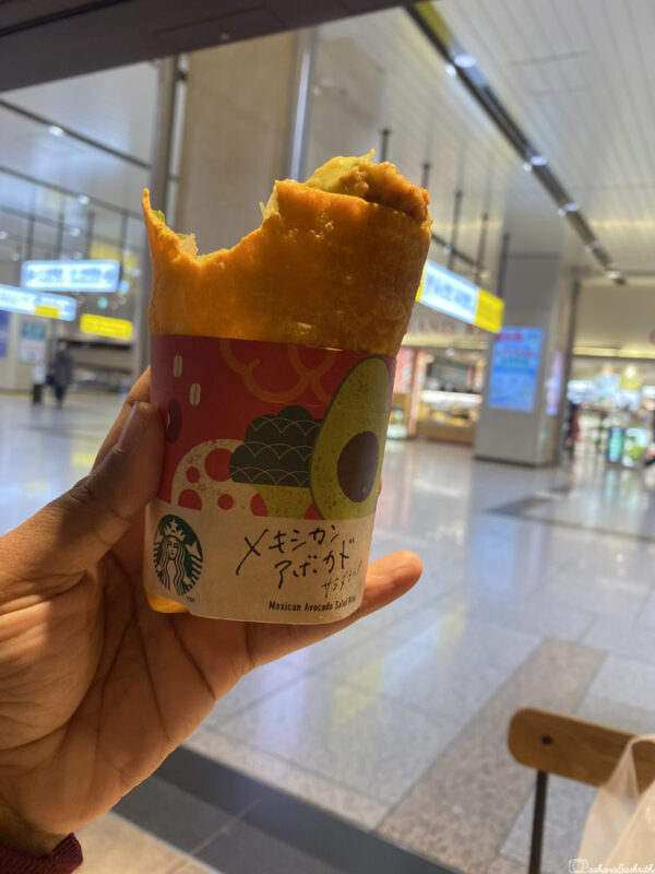 A hand holding a Mexican avocado wrap from Starbucks, set in a bright, indoor location