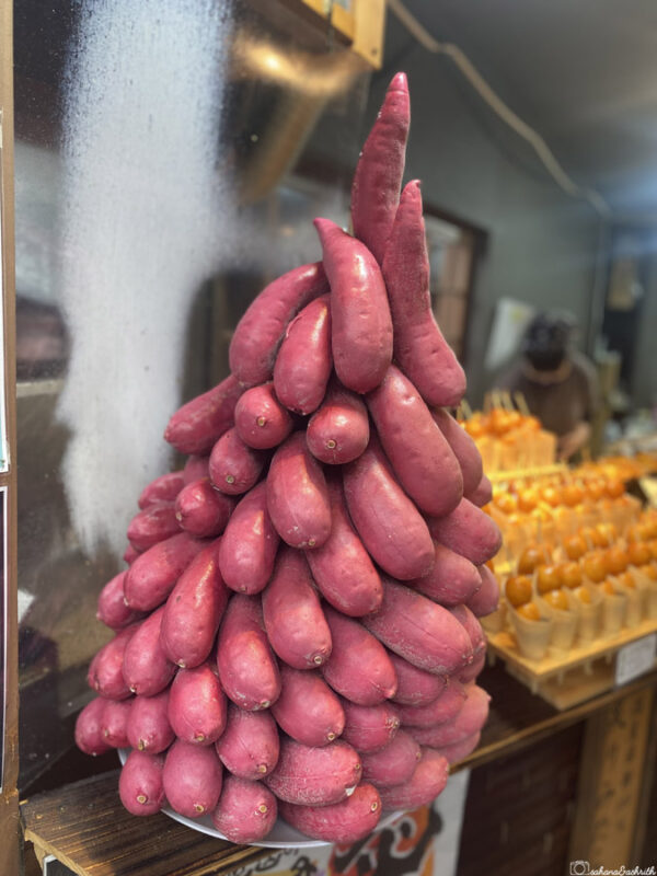  A large, neatly stacked pyramid of purple sweet potatoes displayed at a market stall