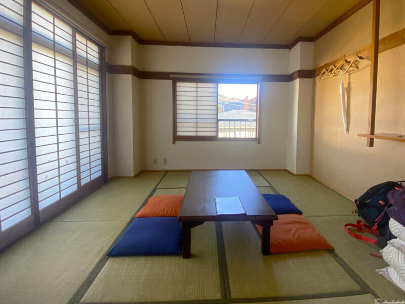 Minimalist Japanese-style room with tatami flooring, a low table, and floor cushions near a window.