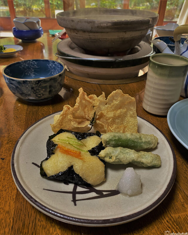 Plate of tempura with seaweed, beans, and vegetable fritters, placed on a wooden table.