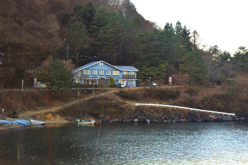 A blue lakeside house  by saiko lake surrounded by trees, located on a small hill.