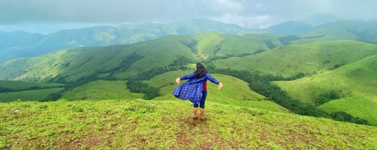 girl standing on the clifsside o mountain peak looking over green rolling hills