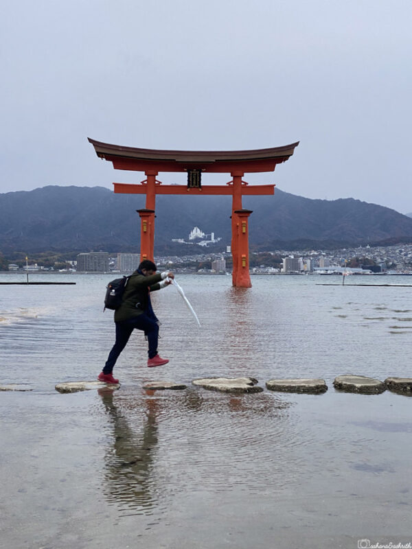 ashrith jumping on stepping stones near the Torii Gate on Miyajima island during low tide with mountains in the background, highlighting playful travel moment