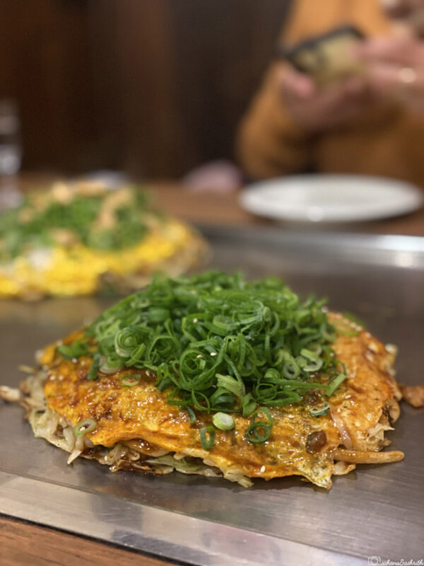 Traditional Hiroshima okonomiyaki served hot on a teppan grill, topped with spring onions, showing a famous Japanese street food dish