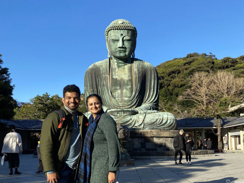 A smiling couple poses in front of the Great Buddha statue (Daibutsu) at Kamakura.