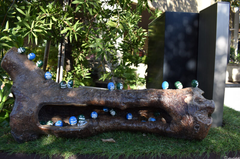 Wooden log with painted stones, each inscribed with blessings, on display at a Kamakura shrine.