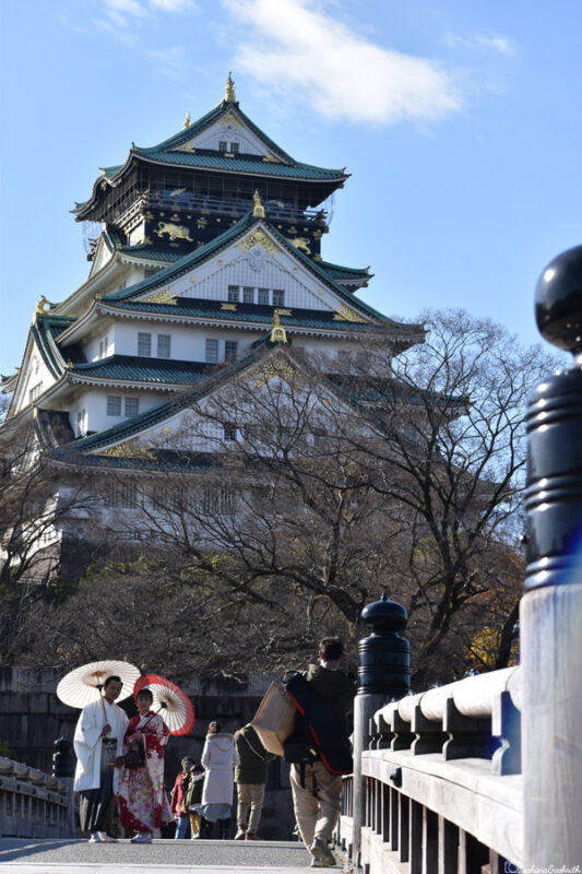 Couple in traditional kimonos walking on the bridge in front of Osaka Castle, a popular spot for cultural experiences in Japan.