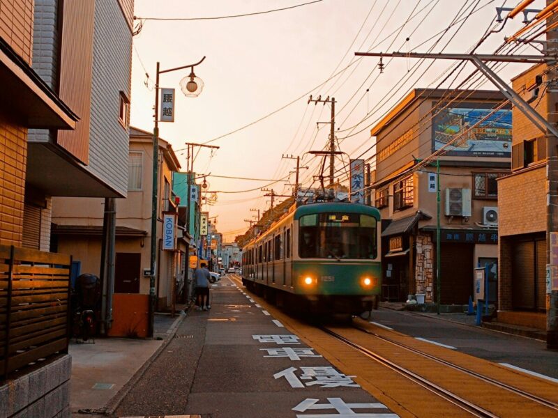 Evening scene of Kamakura's Enoden train passing through narrow streets, capturing the charm of traditional houses and warm sunset tones