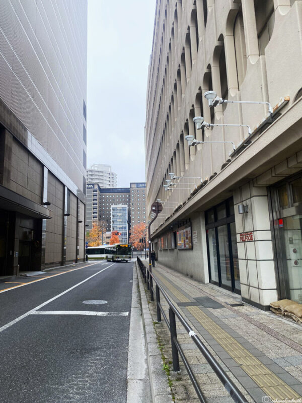 Narrow street between two buildings in Hiroshima, leading toward the main street, with a bus and modern buildings in the background