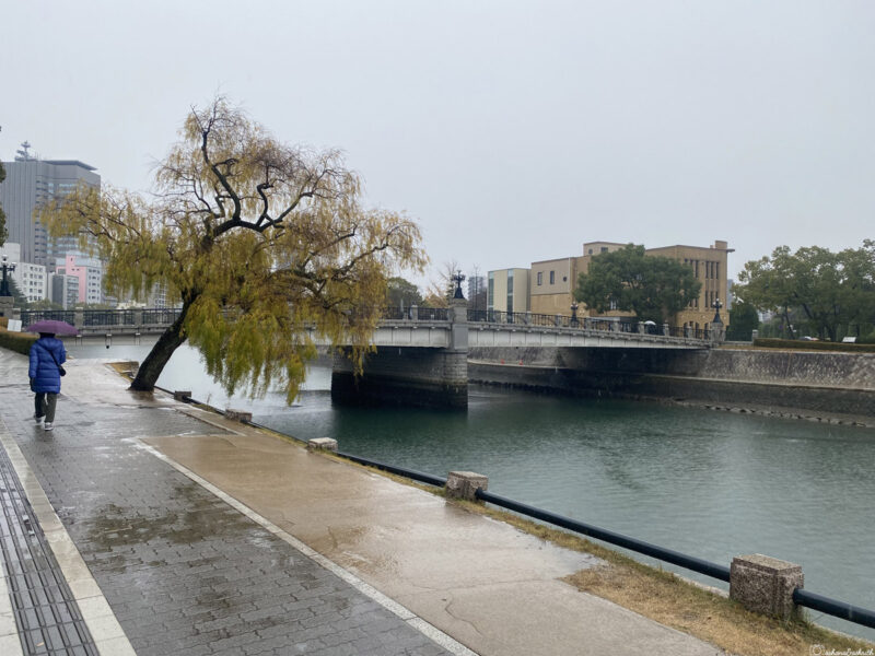 A peaceful scene of the Motoyasu River, with a tree by the riverside and a bridge leading to the Rest House
