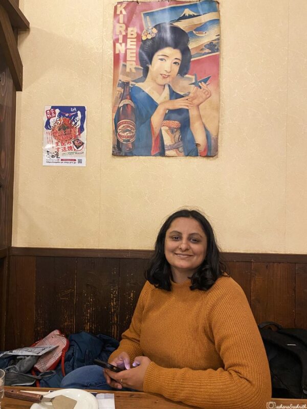 sahana sitting at a cosy nagataya restaurant table with traditional Kirin Beer poster on the wall, enjoying Japanese dining atmosphere