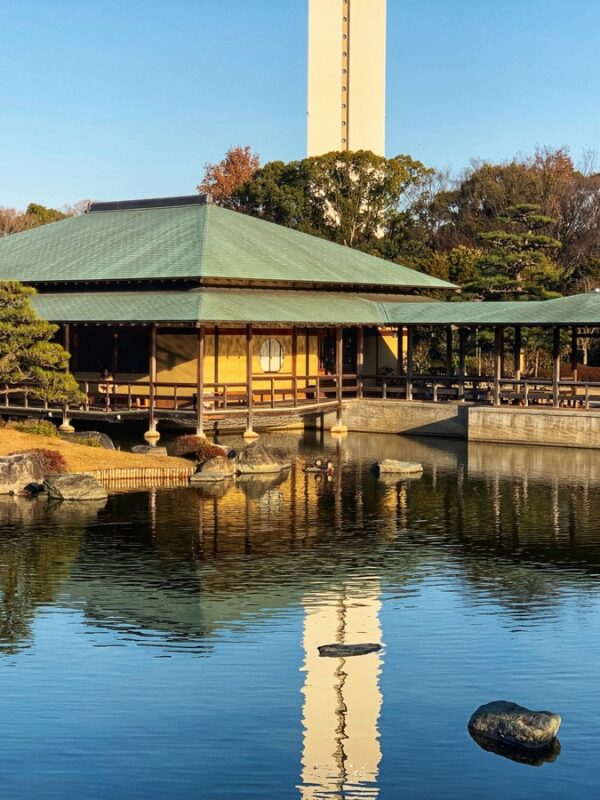 Traditional Japanese tea house at sakai in Osaka, overlooking a calm reflective pond, with trees and a modern high-rise in the distance