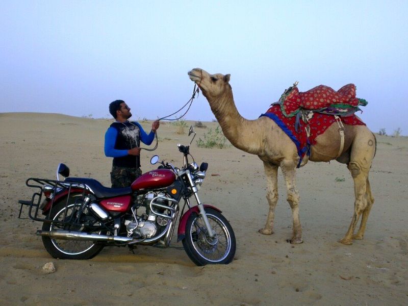 indian biker holding a camel beside his bike on thar desert in Rajasthan, India