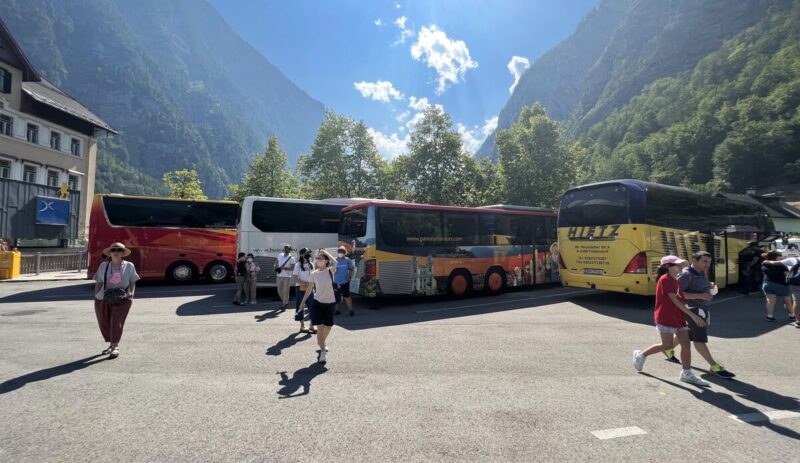 Three big tourist buses parked in Hallstatt parking lot on a sunny afternoon.