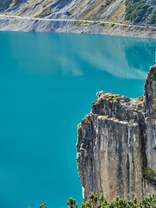 rocky cliff overlooks the vibrant turquoise water of an alpine reservoir in Austria.