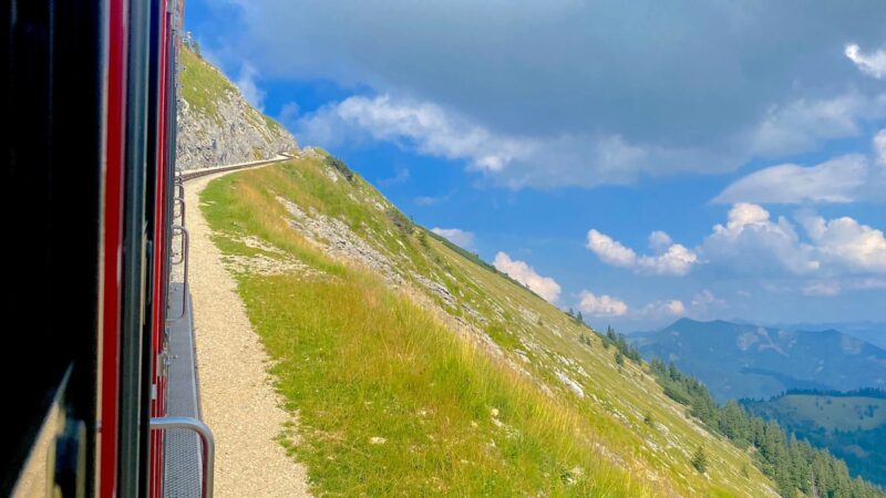 A red train climbs a steep path on Schafberg Mountain with scenic alpine views.