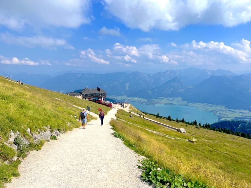 A gravel path leads to a mountain hut with views of Lake Wolfgangsee and distant peaks at schafberg last stop