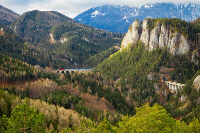 A red train crosses stone viaducts along the Semmering Railway through the Austrian Alps