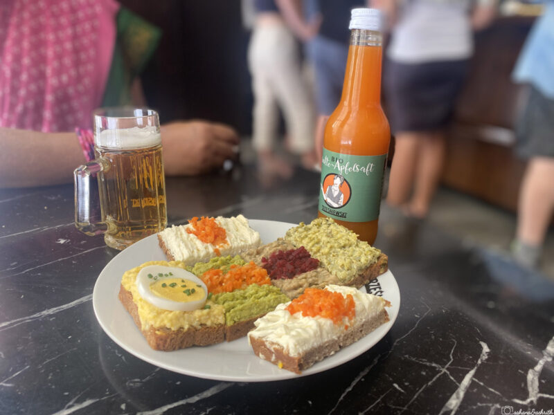 A plate of mini sandwiches with eggs and vegetables, along with carrot juice and a mug of beer, at Trzesniewski, Vienna.