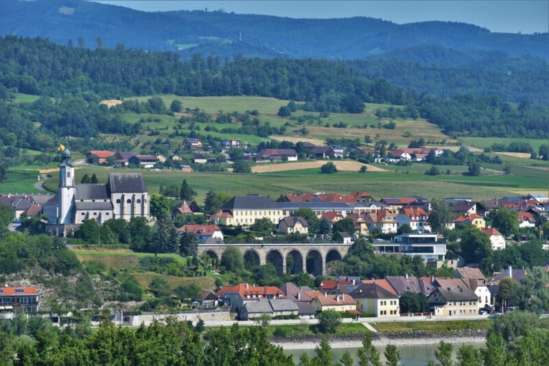 Typical Austrian stone church in a village by the Danube riverside, surrounded by meadows, with a stone bridge on a sunny summer day.