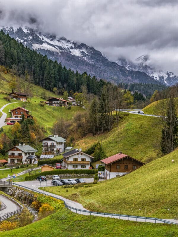 Charming alpine village in Berchtesgaden with traditional houses, green slopes and misty snow-capped mountains in the background