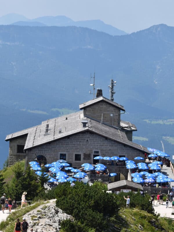 Stone building with a terrace full of blue umbrellas at the Eagle’s Nest, set against the backdrop of distant Bavarian mountains