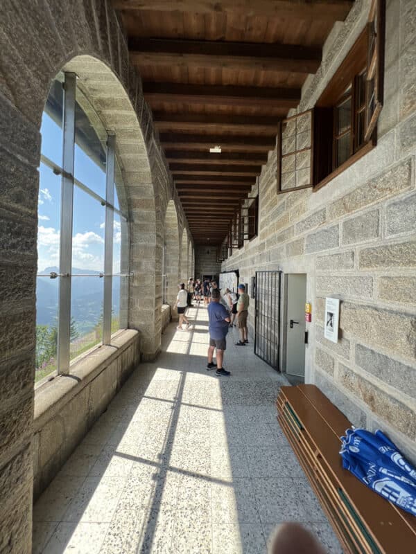 ourists standing along the arched stone corridor inside Eagle’s Nest with mountain views and open windows.