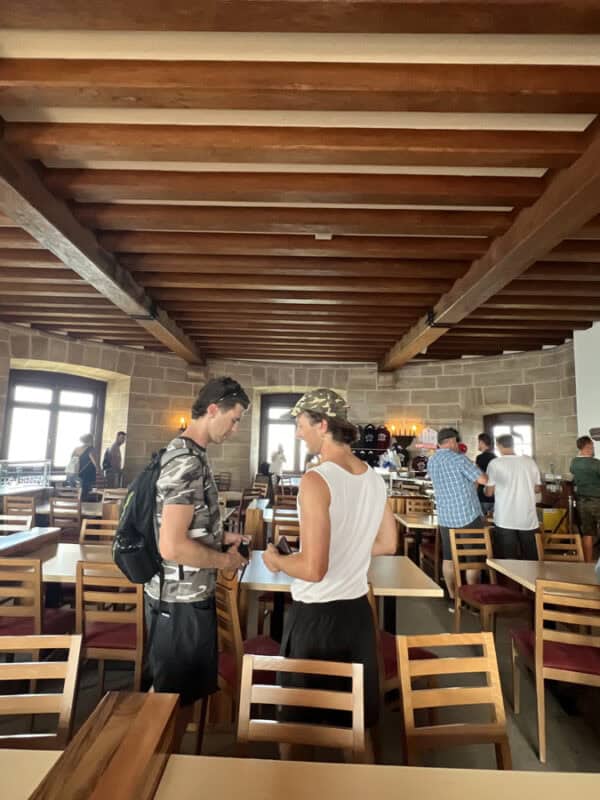 Visitors standing and chatting inside the Eagle’s Nest restaurant, with wooden beams, stone walls and dining tables